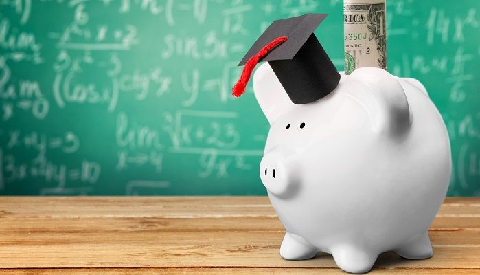 Alcancía con birrete de graduación frente a un tablero con fórmulas financieras